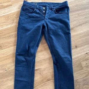 Blå skinny jeans från Dondup - Säljer ett par blå skinny fit jeans från Dondup, modell George. Jeansen har klassisk femficksdesign, knappgylf och är tillverkade i ett mjukt bomullsmaterial. Snygg passform som sitter tight hela vägen ner.
