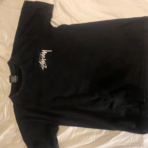 Svart Stüssy t-shirt med tärningar - Svart t-shirt från Stüssy med vit logga på bröstet och stort tryck med tärningar och logga på ryggen. Klassisk rund hals och korta ärmar. Materialet är mjuk bomull, perfekt för streetwear och chill stil.