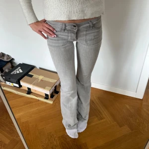 Grå bootcut jeans med låg midja - Säljer ett par ljusgrå jeans med bootcut-modell och låg midja. Jeansen har dubbla silverfärgade knappar framtill. Snygg passform som sitter tajt upptill och släpper vid benen. Jeansen är från Nelly och är en gammal Model som inte fins längre💗💗