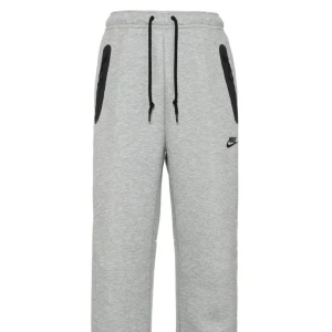 Grå mjukisbyxor från Nike - Snygga grå mjukisbyxor från Nike med svarta dragkedjor på fickorna och svart snörning i midjan. Byxorna har en avslappnad passform och är perfekta för chill eller träning. Nike-logga broderad på ena benet.