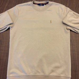 Stickad tröja från Ralph Lauren - En stilren beige tröja från Ralph Lauren med klassisk broderad logga på bröstet och ärmen. Tröjan har inte kommit till användning och ligger bara i garderoben. Har ni funderingar så hojta till bara, priset går alltid att diskutera!