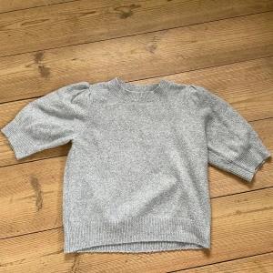 Grå stickad tröja med puffärm från ONLY - Säljer en ljusgrå stickad tröja från ONLY i storlek XS. Tröjan har korta puffärmar och ribbade muddar vid hals, ärmslut och nederkant. Perfekt för dig som gillar en enkel men trendig stil.