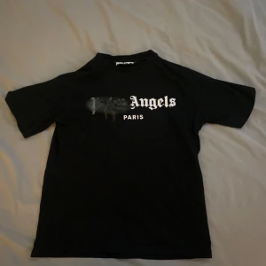 Palm Angels Paris T-shirt – ikonisk streetwear i svart - Säljer en stilren och populär Palm Angels t-shirt i svart med det ikoniska trycket “Paris” och spray-effekten över loggan – en riktig klassiker inom streetwear!  ✅ Originaldesign ✅ Svart med vit logga och spray-detalj ✅ Storlek: S ✅ Passar perfekt för både vardag och fest ✅ Skön passform och snygg stil ✅ I fint skick – använd men välbevarad
