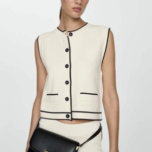 Stickad väst från mango  - Stilren vit väst med svarta kanter och knappar framtill. Västen har två dekorativa fickor och en rak passform. Perfekt för att lyfta en enkel outfit med en klassisk touch. NYPRIS 420kr, storlek M🥰