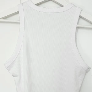 Vit ribbad linnetopp - Säljer en enkel och stilren vit ribbad linnetopp med ärmlös design. Perfekt för varma dagar eller som lager under andra plagg. Tidlös modell med rund halsringning och mjukt material.