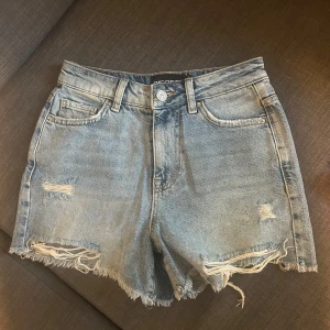 Ljusblå jeansshorts - Säljer ett par ljusblå jeansshorts från Pieces i storlek XS. Shortsen har fransiga benslut, slitna detaljer och klassisk femficksdesign. Perfekta för sommaren och ger en avslappnad look. Säljer då de blivit för små för mig
