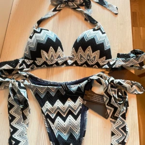 Mönstrad bikini med knyt - snygg bikini, oanvänd med prislappar kvar och zigzag-mönster i svart, vitt och blått. Överdelen har halterneck och knyt i nacken, underdelen har knyt i sidorna. Perfekt för stranden! Pris kan diskuteras vid snabb affär🩷