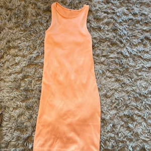  orange  klänning - Säljer en ribbad, ärmlös klänning i en fräsch orange färg. Klänningen har en tight passform och är i midi-längd, perfekt för varma dagar. Materialet är stretchigt och bekvämt, vilket gör den enkel att bära hela dagen.