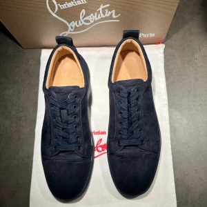Mörkblå sneakers från Christian Louboutin - Snygga mörkblå sneakers i mocka från Christian Louboutin med den ikoniska röda sulan. Skorna har snörning och en stilren design som passar perfekt för en trendig look. Skick: 9.5/10 ✨ Använda 1-2 gånger. De är storlek 42 men de passar 41 också. Lite använda och smutsiga men kommer att göra rent dom innan jag säljer👍