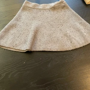 Grå stickad kjol från Zara - Supermjuk och ribbstickad grå kjol från Zara. Kjolen har en lätt utställd form och är perfekt för dig som gillar en enkel men snygg stil. Passar till många olika outfits och är riktigt skön att ha på sig.