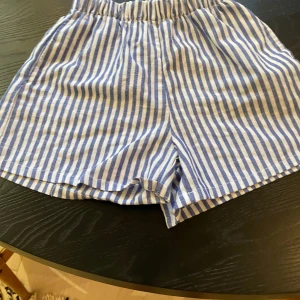 Blåvitrandiga shorts från SHEIN - Säljer ett par blåvitrandiga shorts från SHEIN med elastisk midja. De är tillverkade i ett lätt och luftigt tyg, perfekta för varma dagar. randigt mönster