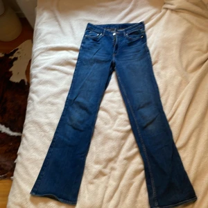 Blå bootcut jeans från &Denim - Säljer ett par klassiska blå bootcut jeans från &Denim med hög midja. Jeansen har fem fickor, dragkedja och knapp framtill. Perfekta för dig som gillar en tidlös denimlook med lite utsvängda ben.