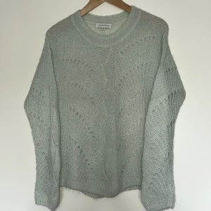 Ljusgrön stickad tröja från Second Female - Mysig ljusgrön stickad tröja från Second Female i storlek XS. Tröjan har ett diskret hålmönster och rund halsringning. Perfekt för lager-på-lager och passar till många olika stilar. 40% polyamid, 32% mohair, 28% ull