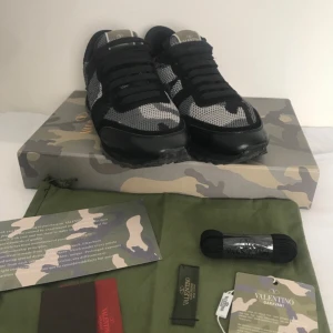Valentino Rockrunner sneakers i svart och grått - Säljer ett par Valentino Rockrunner sneakers med svart och grått camouflage-mönster. Skorna har svarta snören, mesh och mockadetaljer samt en platt sula. Kommer med originalkartong och tillbehör.