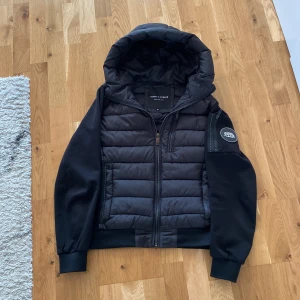 pufferjacka från Supply & Demand ny 1000 - Säljer en svart pufferjacka från Supply & Demand och dragkedja. Jackan har quiltad framsida, mjuka ärmar och en patch på ena ärmen. Perfekt för kyliga dagar och snygg streetstil.