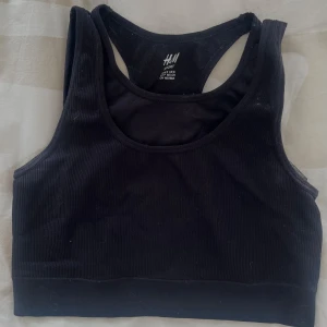 Svart ribbad sport-bh från H&M - Svart ribbad sport-bh från H&M med brottarrygg. Mjuk och stretchig modell som passar perfekt till träning. Enkel och stilren design utan synliga detaljer eller mönster.