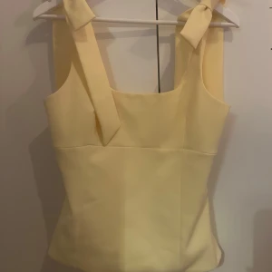 Gul linnetopp med rosettband - Säljer denna söta gula toppen från Zara. Slutsåld i butik och online, väldigt efterfrågad. Aldrig använd lappen är kvar. En liten sminkfläck längst ner på tröjan(syns på sista bilden). Hör av er vid frågor❣️