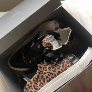  Sneakers  - Säljer ett par snygga sneakers med leopardmönster och svarta detaljer. Skorna har svarta snören, svarta glansiga detaljer och vit sula. Perfekta för dig som vill skapa en trendig look! 