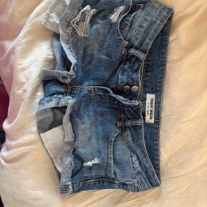 Blå jeansshorts med slitningar från True North - Säljer ett par blå jeansshorts från True North med snygga slitningar och råa kanter. Shortsen har klassisk femficksdesign, knappgylf och låg midja. Perfekta för varma dagar och en avslappnad stil.