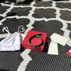 Grönt armband med nitar från Valentino Garavani - Snyggt grönt armband från Valentino Garavani i skinn med silverfärgade pyramidformade nitar. Just denna färgen på armbandet är helt slutsålt överallt och tror ja är den enda på plick med just denna!🙌🏼 Bara att skriva vid funderingar! Bytesförslag kan va intressant! Har fler äkthetsbevis!