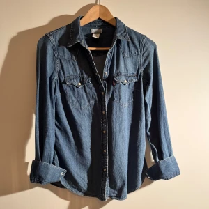 Jeansskjorta  - Säljer en klassisk blå jeansskjorta från Levi's med knappar och två bröstfickor. Skjortan har flera snygga detaljer vilket gör den unik. Vid frågor eller funderingar är det bara att skriva!