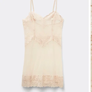  spetsklänning nattlinne med smala axelband - Säljer en elegant champagnefärgad klänning med tunna axelband och vackra spetsdetaljer framtill och nedtill. Klänningen har en feminin v-ringning och är tillverkad i ett lätt, syntetiskt material som ger en mjuk känsla. Tvättas innan den skickas bara använd 2 gånger. 