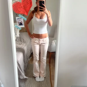 Ljusrosa jeans med broderade detaljer från Miss Me - Säljer ett par ljusrosa jeans från Miss Me med snygga broderade kors och silverdetaljer på bakfickorna. Byxorna är omsydda vid benen för att vara bootcut och har låg midja. Perfekta för dig som vill sticka ut lite extra!