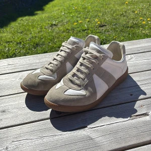 Maison Margiela Gats - Säljer ett par stilrena gats i vitt och beige med snygga mockadetaljer och klassisk design. Skorna har rund tå, platt sula och snörning. Perfekta för dig som gillar en clean och tidlös look.