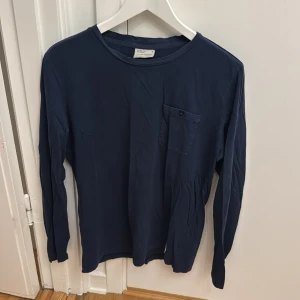 Mörkblå långärmad tröja från Peak Performance - Säljer en stilren mörkblå långärmad tröja från Peak Performance i storlek M. Tröjan har en rund halsringning och en bröstficka med knapp. Perfekt för en avslappnad och enkel look.
