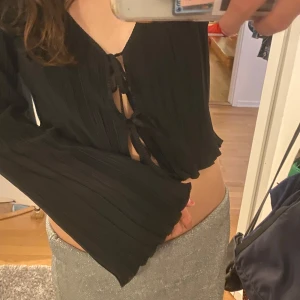 Svart croppad blus med knyt framtill - Trendig svart croppad blus med långa vida ärmar och knytning framtill. Blusen har en djup v-ringning och är tillverkad i ett ribbat material. Pris kan diskuteras