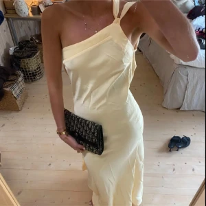 Gul balklänning - Säljer en ljusgul långklänning med oneshoulder och knyt vid axeln. Klänningen har en elegant och enkel design med mjuka linjer och är perfekt för sommarens tillfällen. Materialet känns lätt och följsamt mot kroppen. Jag är 176 cm lång och brukar ha xs/s. Inga defekter, helt ny