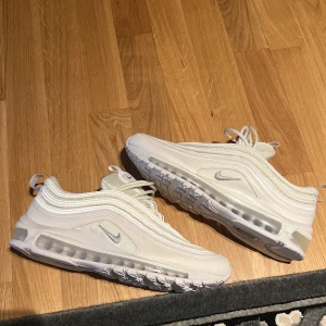 Nike Air Max 97 vita sneakers - Säljer ett par fräscha Nike Air Max 97 i helvitt med silvriga detaljer. Skorna har den klassiska vågiga designen, synlig Air Max-sula och snörning. Perfekta för dig som gillar stilrena och sportiga sneakers. Skorna är endast prövade inomhus. 