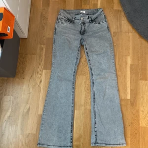 Ljusgrå bootcut jeans - Säljer ett par ljusgrå bootcut jeans med klassiska fem fickor och svarta sömmar. Snygga detaljer på bakfickorna med broderade mönster. Jeansen är från Nelly med ett stretchigt matrial. Jag säljer för jag inte riktigt använt de😊