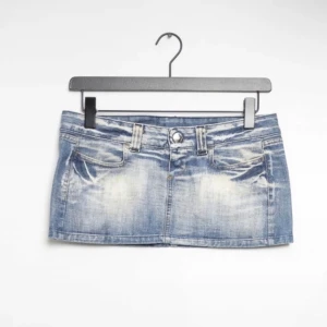 Blå jeanskjol mini - Säljer en klassisk blå jeanskjol i minilängd med slitna detaljer och femficksdesign. Kjolen har bälteshällor, knapp och dragkedja framtill samt bakfickor. Perfekt för en avslappnad och trendig look.
