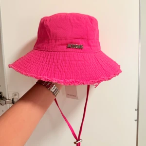 Jacquemus bucket hat - Säljer en helt ny och oanvänd Jacquemus solhatt i stark rosa färg. Trendigt bred brätte med fransad kant och justerbart hakband – perfekt för sommaren! Äkta vara med metallogo framtill.  Skicka PM vid intresse!