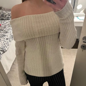 Beige offshoulder tröja - Säljer en snygg beige offshoulder tröja med ribbad design. Tröjan har långa ärmar och en bekväm passform som passar perfekt för både vardag och fest. Perfekt för att hålla stilen under kyligare dagar.Har ett litet hål på baksidan men som knappt syns