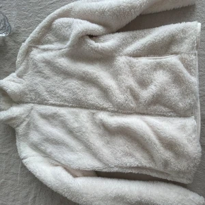 Vit teddyjacka från Primark - Mysig vit teddyjacka från Primark i storlek S. Perfekt för kyliga dagar med sin fluffiga och mjuka textur. Jackan har långa ärmar och en enkel design utan krusiduller.