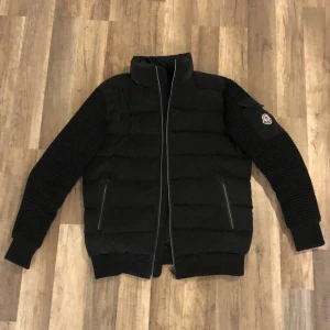 Svart dunjacka från Moncler - Snygg svart dunjacka från Moncler med quiltad design och dragkedja framtill. (Använt endast 1 gång) Jackan har långa ärmar med ribbade detaljer och en broderad logotyp på ärmen. Perfekt för kyligare dagar under våren. Går att frakta mot swish.