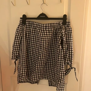 Rutig sommartopp  - Säljer en söt rutig topp i svart och vit. Toppen har en omlott-design med knytband i sidan som ger en fin detalj. Perfekt för en avslappnad och stilren look.