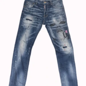 Dsquared byxor - Unika blå jeans från Dsquared2 med ett iögonfallande tryck av ett ansikte och slitna detaljer. Jeansen har en knappgylf och små vita färgstänk för en unique design. Jag försöker sälja den för att jag har ändrat min stil.
