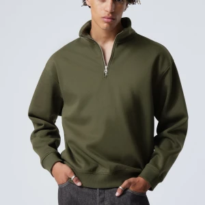 Olivgrön tröja med dragkedja - Snygg olivgrön tröja med halv dragkedja och hög krage. Perfekt för en avslappnad stil. Tröjan har långa ärmar och ribbade muddar vid ärmslut och nederkant.