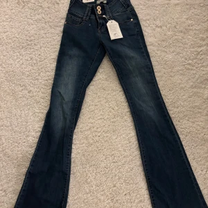 Mörkblå jeans med väldigt låg midja från infinyparis - Snygga mörkblå jeans från infinyparis som är väldigt låg midja de  och tre dekorativa knappar framtill. Klassisk femficksdesign och en liten logga på bakfickan. Aldrig använda!!