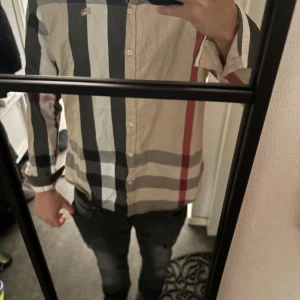 Burberry skjorta - Snygg rutig skjorta med långa ärmar i beige, svart, vit och röd. Skjortan har knappar framtill och en klassisk krage. Perfekt för en stilren look.  Pris går att diskutera🤝