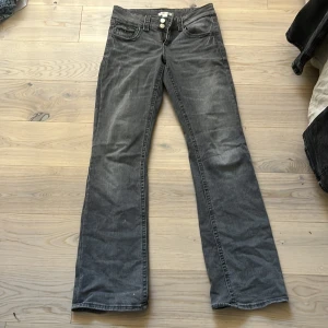 Grå jeans från Gina Tricot - Snygga grå jeans från Gina Tricot med bootcut-stil. De har en låg midja och stängs med två knappar framtill. Perfekta för en avslappnad look.