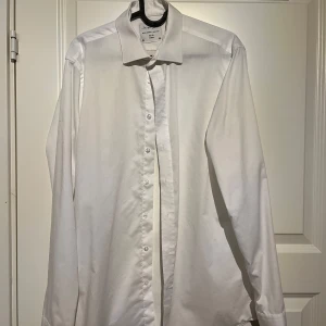 Vit skjorta från Seven Seas - Seven Seas Slim Fit Skjorta – Medium 👕✨  Uppgradera din garderob med denna stilrena och högkvalitativa skjorta från Seven Seas! Tillverkad i 100 % mjuk och andningsbar bomull 🌿, vilket ger både komfort och en snygg look. Den slim fit-passformen ger en modern och smickrande silhuett, perfekt för både jobb och vardag 👌.  ✅ Märke: Seven Seas ✅ Material: 100 % bomull ✅ Passform: Slim Fit ✅ Storlek: Medium ✅ Skick: Mycket bra skick!  