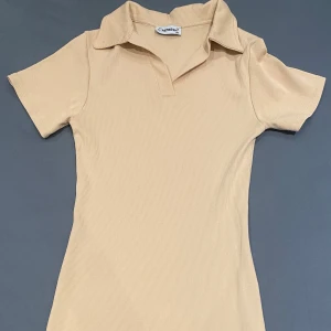 Beige ribbad klänning från Refresh - Storleken är M men är som xs. Säljer en stilren beige klänning från Refresh. Den är ribbad med korta ärmar och en klassisk krage. Perfekt för en avslappnad men ändå elegant look. Passar bra till både vardag och speciella tillfällen.