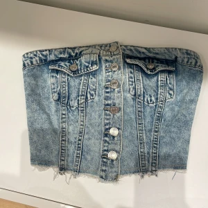 Jeans korsett med knappar, aldrig använt. Storlek XS - Säljer jeans korsett med knappar framtill och fransig nederkant. Den har en elastisk rygg för bättre passform.