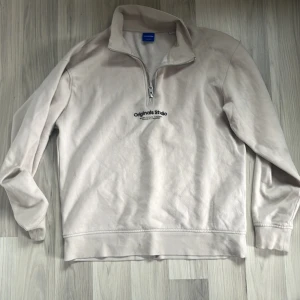 Beige tröja från Jack & Jones - Säljer en beige tröja från Jack & Jones med dragkedja vid halsen och texten 'Originals Style' på bröstet. Tröjan har långa ärmar och är perfekt för en avslappnad stil. Passar bra till både jeans och chinos.