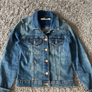 Blå jeansjacka med knappar - Snygg blå jeansjacka med klassisk design och knappar framtill. Jackan har två bröstfickor med knappdetaljer och långa ärmar. Perfekt för en avslappnad stil.💓