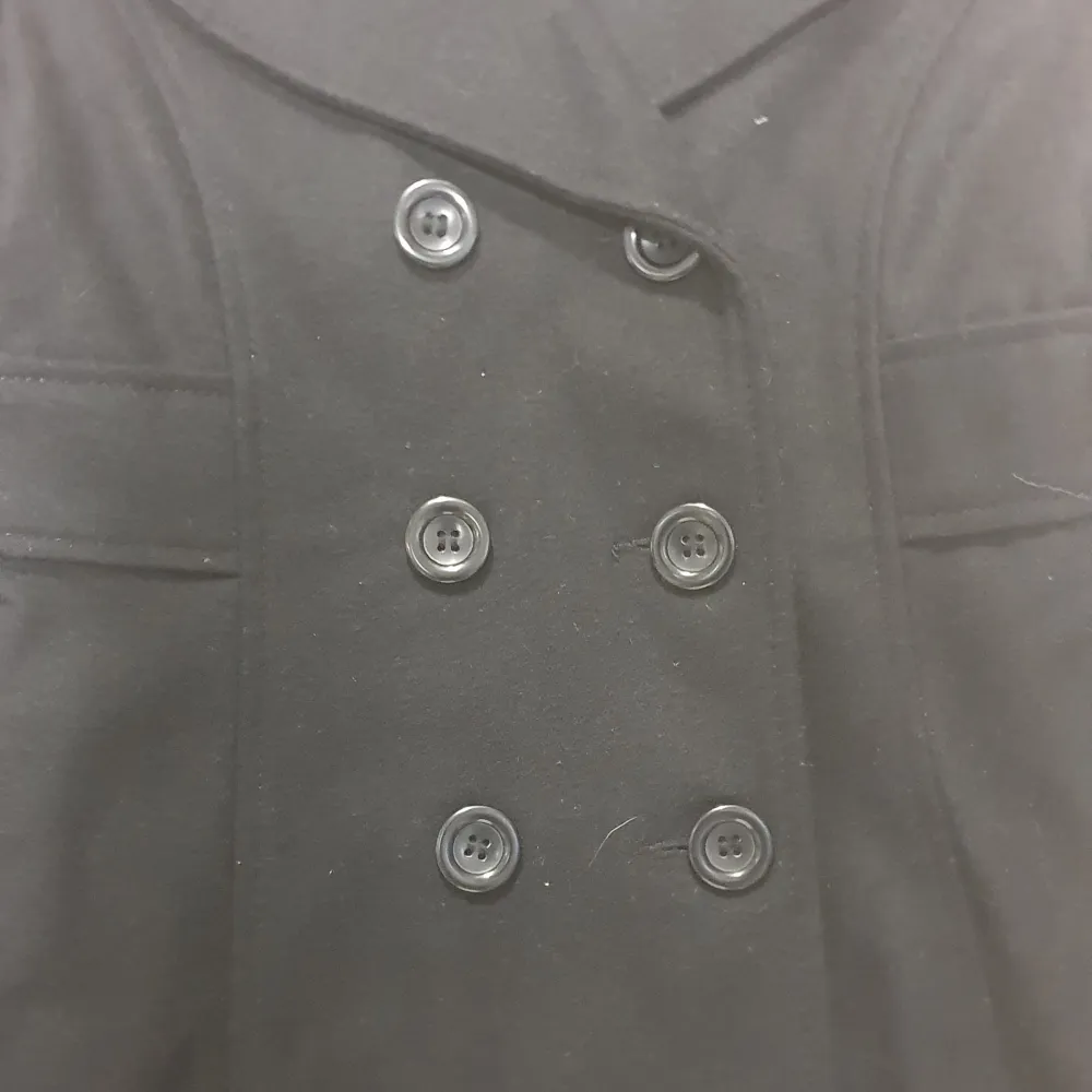 Snygg svart kappa från Lindex med dubbelknäppning och klassisk krage. Perfekt för kyligare dagar med sin stilrena design och praktiska knappar. Ett måste i garderoben för en elegant look.. Takit.
